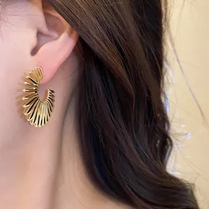 Elegant woman wearing textured gold C-shaped geometric hoop earrings in a close-up shot