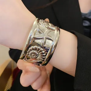 Detailed view of silver-tone starfish and seashell embossed wide metal cuff bracelet