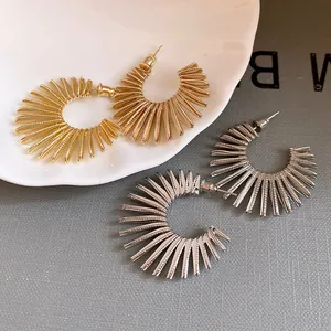 Detailed view of textured sunburst C-shaped earrings in gold and silver finishes