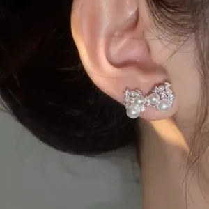 Close-up view of elegant pearl bow earrings with sparkling zircon accents on ear.