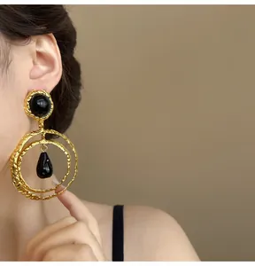 Detailed close-up of vintage gold textured circle earrings with black pendants on model.