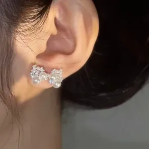 Close-up detail of silver needle zircon pearl bowknot earrings worn on the earlobe.