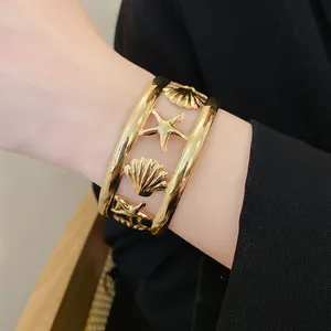 Detail showing the intricate gold starfish and seashell carvings on a hollowed-out cuff bracelet.