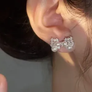 Detailed view of elegant silver bow stud earrings with pearls and zircons on an ear