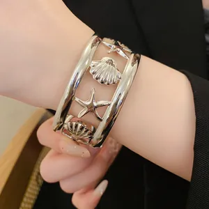 Close-up of a silver starfish and seashell hollow cuff bracelet worn on wrist