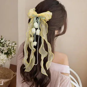 Dettaglio del fermaglio per capelli a fiocco in chiffon giallo con pendenti a tulipano e perle.