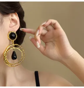 Close-up detail of retro exaggerated gold hoop earrings with black teardrop pendant