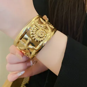 Detailed view of a luxury gold starfish and seashell embossed wide cuff bracelet on wrist