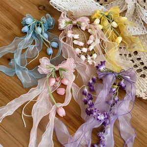 Dettaglio di fermagli per capelli in chiffon colorati con fiori e nappe di perle.