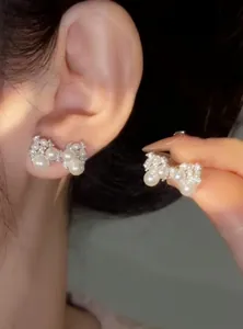 Close-up detail of elegant pearl and zircon bow stud earrings shown worn on an ear
