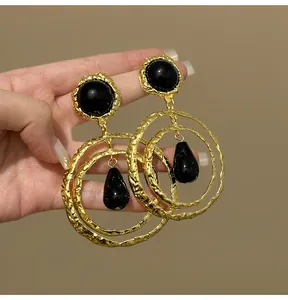 Detailed view of retro hammered gold hoop earrings with black cabochons and drops