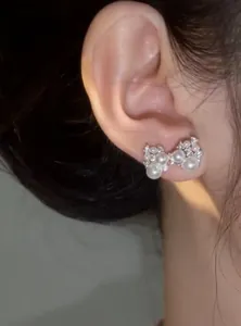 Macro detail showing a delicate silver bow earring with pearls and zircons worn on ear.