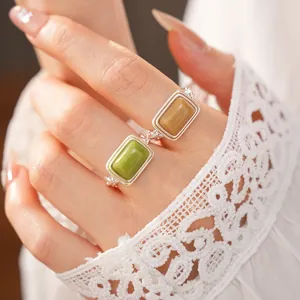 Detail of square resin open rings in green and tan worn on a hand with lace sleeve