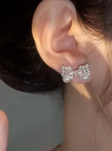 Close-up of elegant silver needle bow-knot stud earring with pearls and zircon on ear