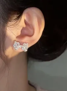 Detailed close-up showing silver zircon pearl bow earrings worn on a model's ear lobe
