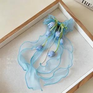 Primo piano del fermaglio per capelli con fiocco in chiffon blu, tulipani e perle.