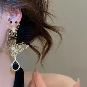 Close-up of gold butterfly earring with black teardrop pendant on female model.