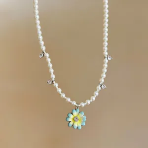 Detailed view of the beaded pearl necklace with blue enamel flower and heart zircon charms
