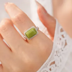 Detail view of a square green resin ring worn on a finger with lace sleeve background