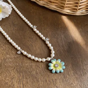 Detailed macro view of gradient enamel flower pendant and heart charms on a pearl necklace