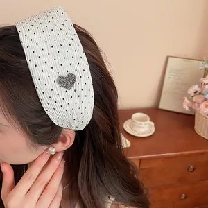 Close-up of a white polka dot headband with a rhinestone heart on a model.