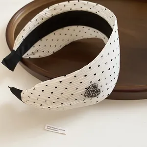 Macro view of a white pleated polka dot headband with a rhinestone heart charm