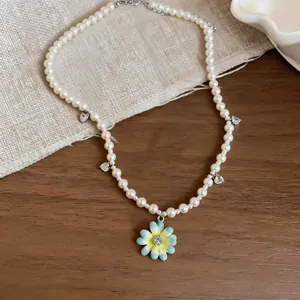 Detailed view of pearl necklace with blue flower pendant and heart zircon charms