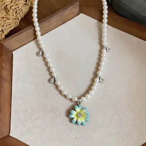 Close-up of a delicate pearl necklace featuring a colorful enamel daisy pendant and zircons
