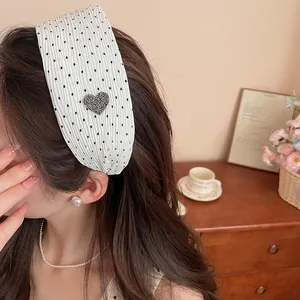 Detailed view of a white polka dot wide headband with a sparkling rhinestone heart decoration.