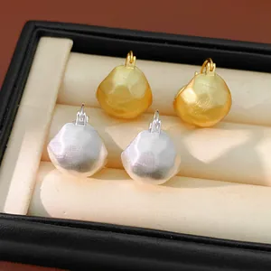 Macro detail of brushed gold and silver geometric half-round earrings in a box.