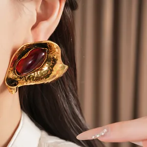 Detail view of large gold-tone geometric stud earrings with a striking red resin stone inlay.
