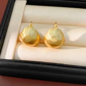 Close-up macro shot of gold brushed geometric ear buckles in a luxury jewelry box