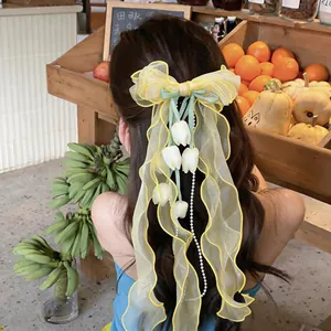 Dettaglio di un fermaglio per capelli con fiocco in chiffon giallo e nappe di perle