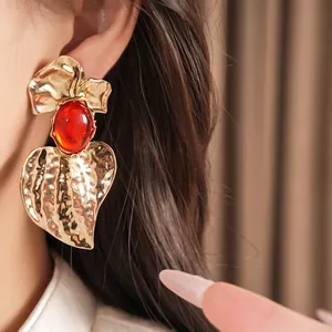 Detail view of bold gold hammered leaf earring with a vibrant red resin stone