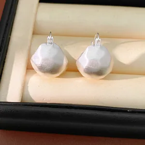 Detailed macro shot of silver-colored brushed geometric metal ear clips in a box.