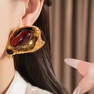 Detailed close-up of exaggerated gold geometric earring with red oval resin stone