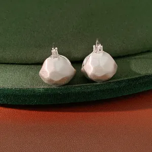 Detail shot of brushed silver-colored geometric semi-circular huggie earrings on green velvet