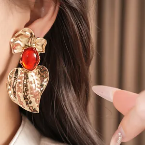 Close-up of oversized hammered gold earrings with elegant red resin oval stone detail