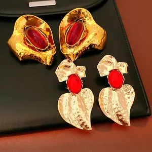 Close-up of vintage hammered gold earrings with red resin stones on black leather.