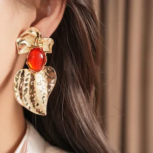 Close-up detail of golden hammered geometric earrings featuring a bold red oval resin center