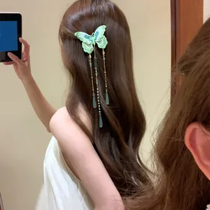 Détail d'une pince à cheveux papillon tricoté vert avec de longs glands perlés