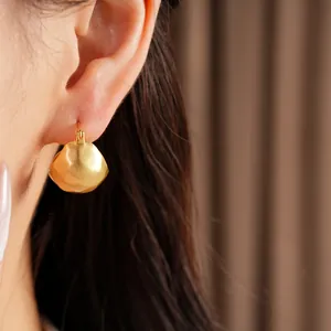 Detail view of golden brushed geometric semi-circle earrings on a model's ear.