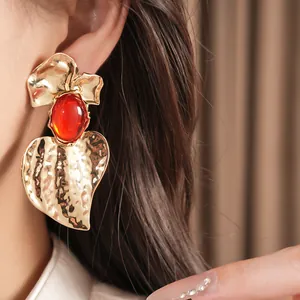 Close-up detail of gold hammered leaf earring with red oval resin stone worn on ear