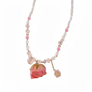 Delicate glass beaded necklace featuring a pink preserved rose pendant on a white background.
