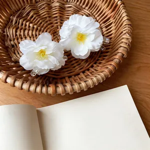 Detailed view of two white fabric flower hair claw clips placed in a wicker basket.
