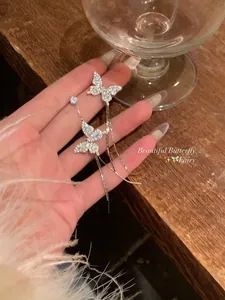 Detailed view of sparkling silver asymmetrical butterfly tassel earrings held in hand