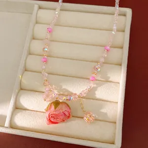 Detail showing pink beaded necklace with a preserved rose pendant on a jewelry tray.