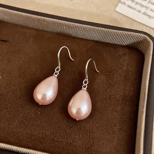 Close-up of peach water-drop pearl earrings resting in a brown velvet jewelry box