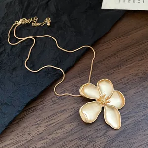 Elegant close-up detail of a vintage gold flower pendant with a thin snake chain necklace.