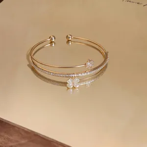 Dettaglio di bracciale rigido dorato a doppio strato con zirconi e quadrifoglio